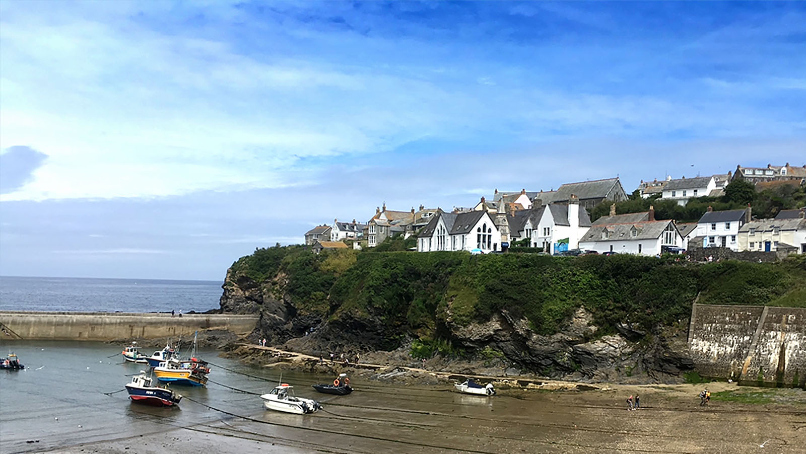 Port Isaac harbour at low tide, with boats on the sand below the clifftop cottages