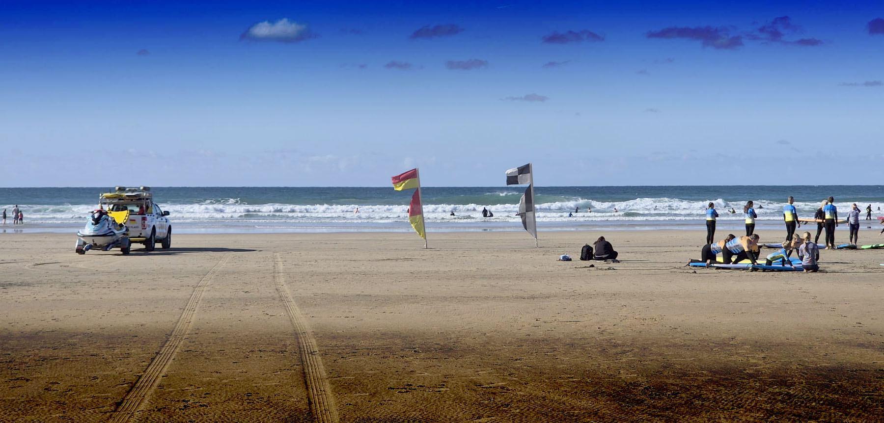 An RNLI lifeguard vehicle on Perranporth beach beside a surf school lesson